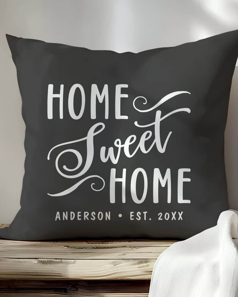 Dark gray throw pillow with the text Home Sweet Home in a stylized white script font. A personalized name and date are also included.
