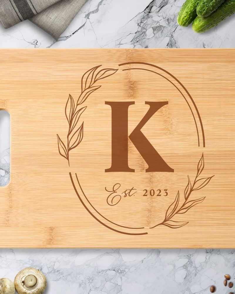 Light brown bamboo cutting board with a brown engraved monogram of the letter K, within a wreath design and the text Est. 2023.