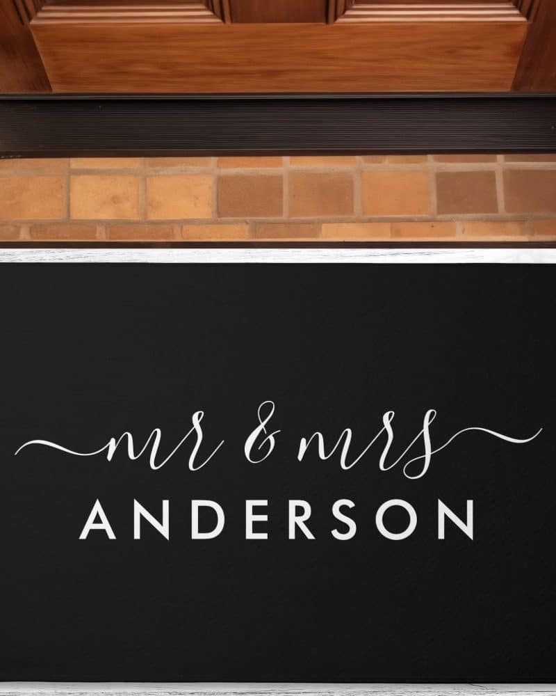 Black welcome mat with the words Mr & Mrs Anderson in white script lettering.