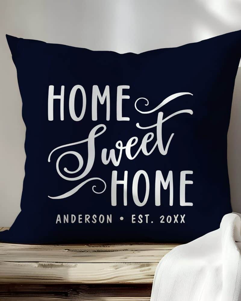 Navy blue throw pillow with the text Home Sweet Home in a stylized white script font. A name and year are also printed at the bottom.