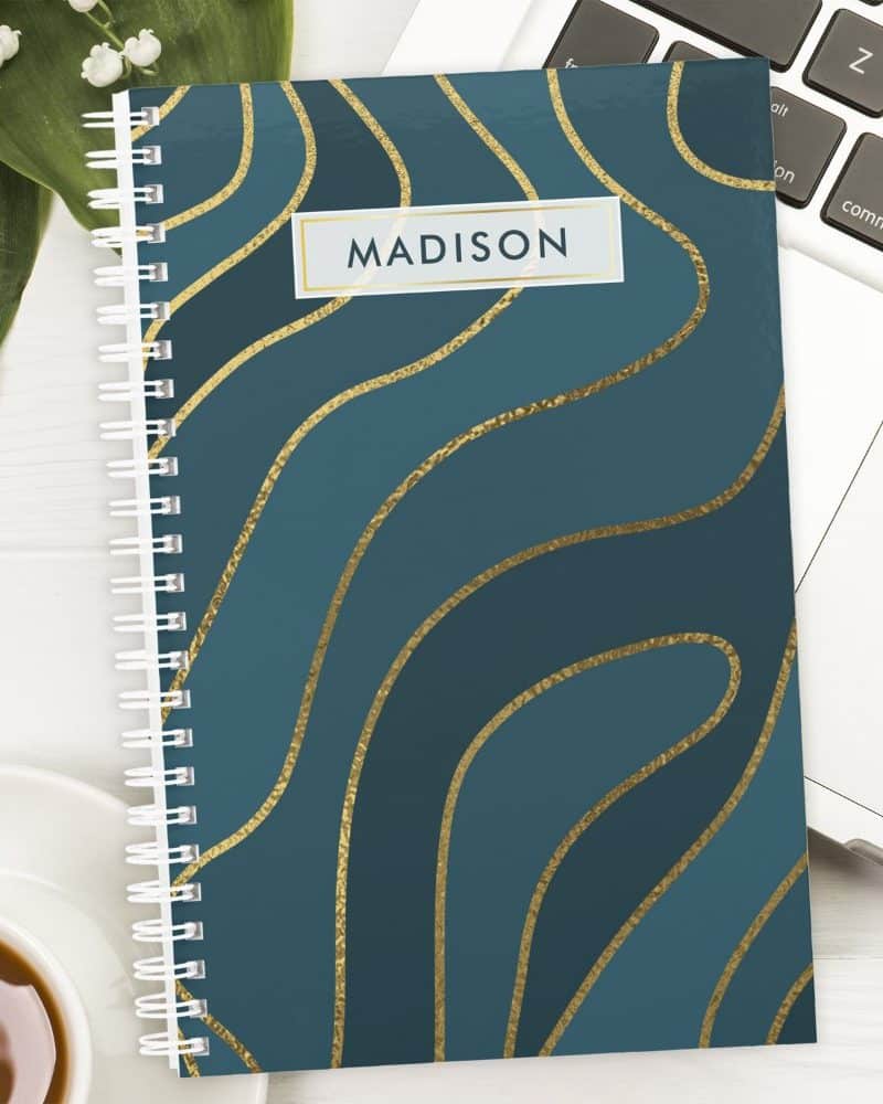 Teal spiral notebook with gold wavy lines and the name Madison on the cover.