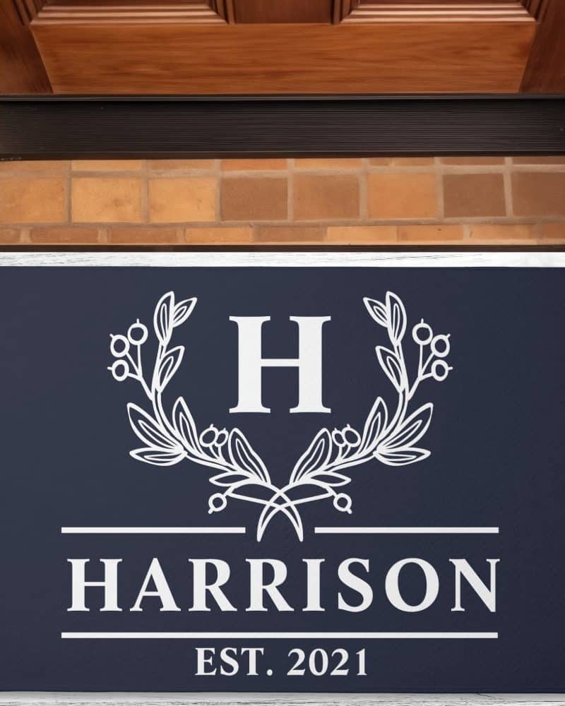 Navy blue doormat with a white monogram featuring the letter H surrounded by an olive branch wreath, the name Harrison, and established 2021.