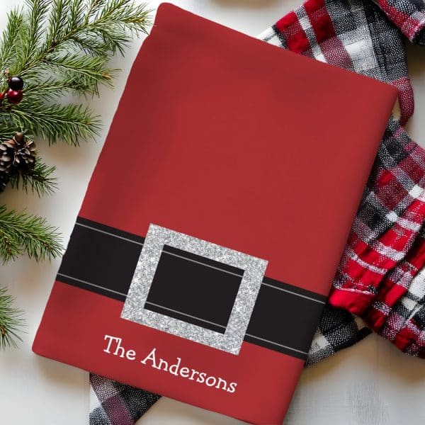 Red Christmas-Themed Kitchen Towel With A Black Belt Buckle Design, Personalized With The Name The Andersons.