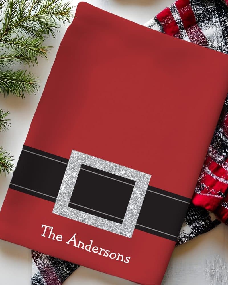 Red Christmas-themed kitchen towel with a black belt buckle design, personalized with the name The Andersons.