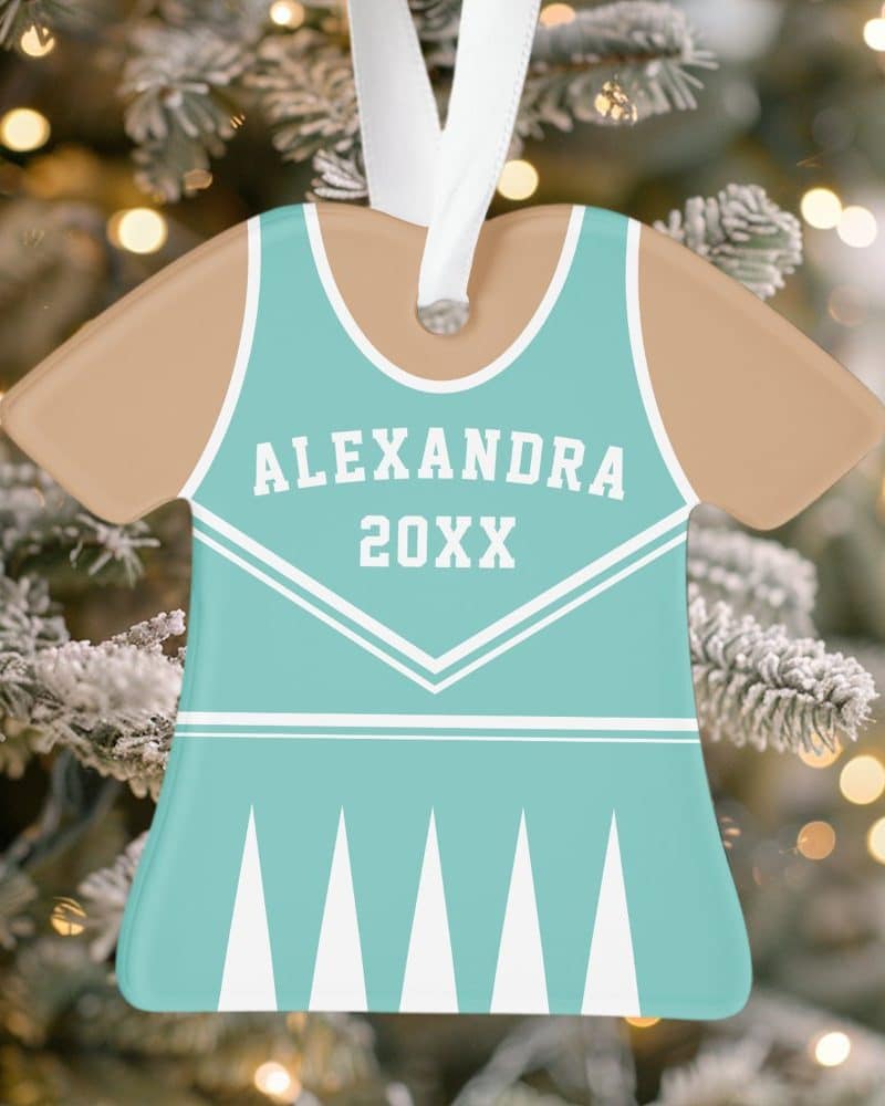 A teal and tan Christmas ornament shaped like a cheerleading uniform, personalized with the name Alexandra and the year 20XX.