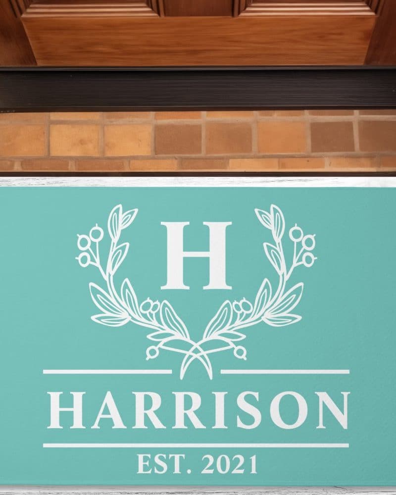 Teal doormat with a white monogram: the letter H in a wreath design, the name Harrison, and established 2021.