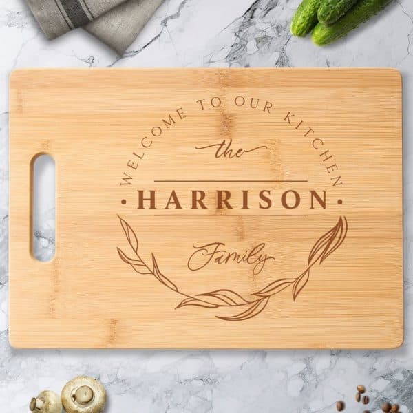 Personalized Bamboo Cutting Board With The Words Welcome To Our Kitchen, The Harrison Family, And A Decorative Leaf Design.