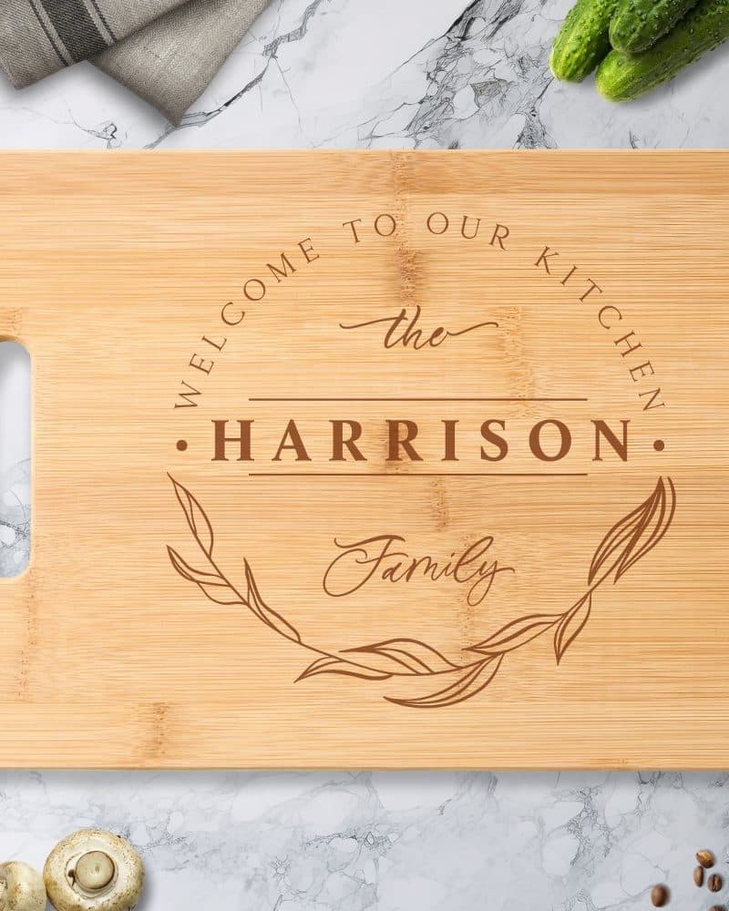 Personalized bamboo cutting board with the words Welcome to our Kitchen, the Harrison Family, and a decorative leaf design.