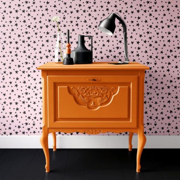 Orange Painted Chest Of Drawers Against A Pink Wall With A Black Star Pattern.