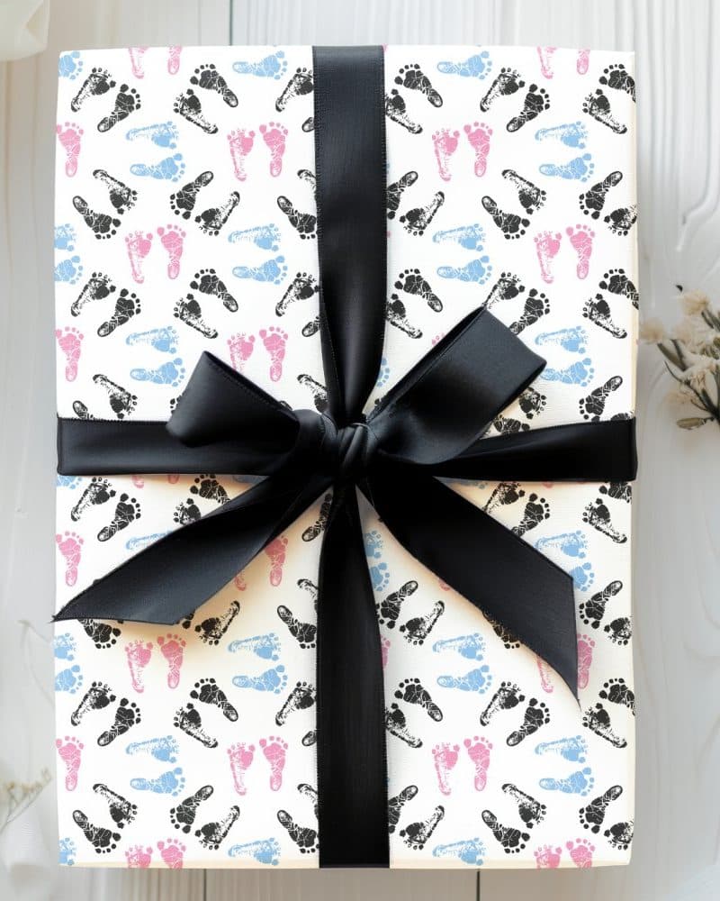 Gift wrapped in white paper with a black ribbon and a pattern of pink, blue, and black baby footprints.
