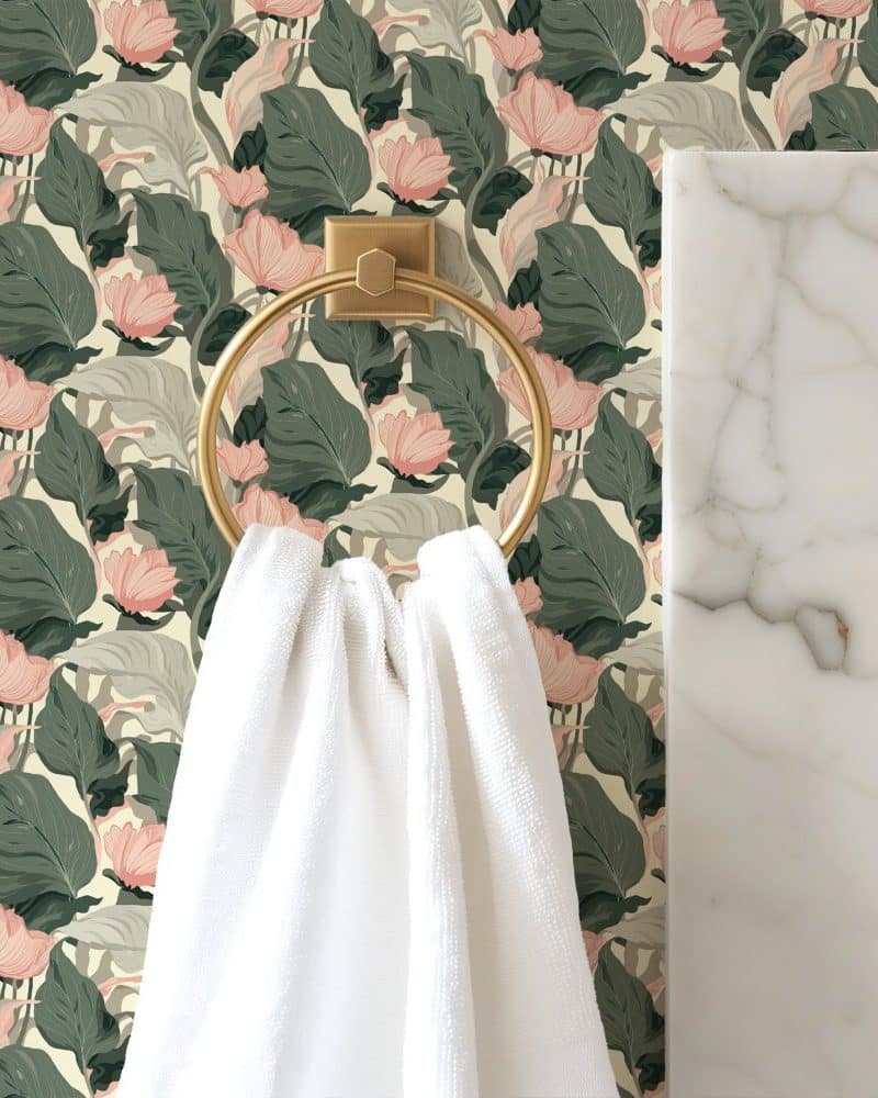 White towel hanging on a gold ring against a floral wallpaper.