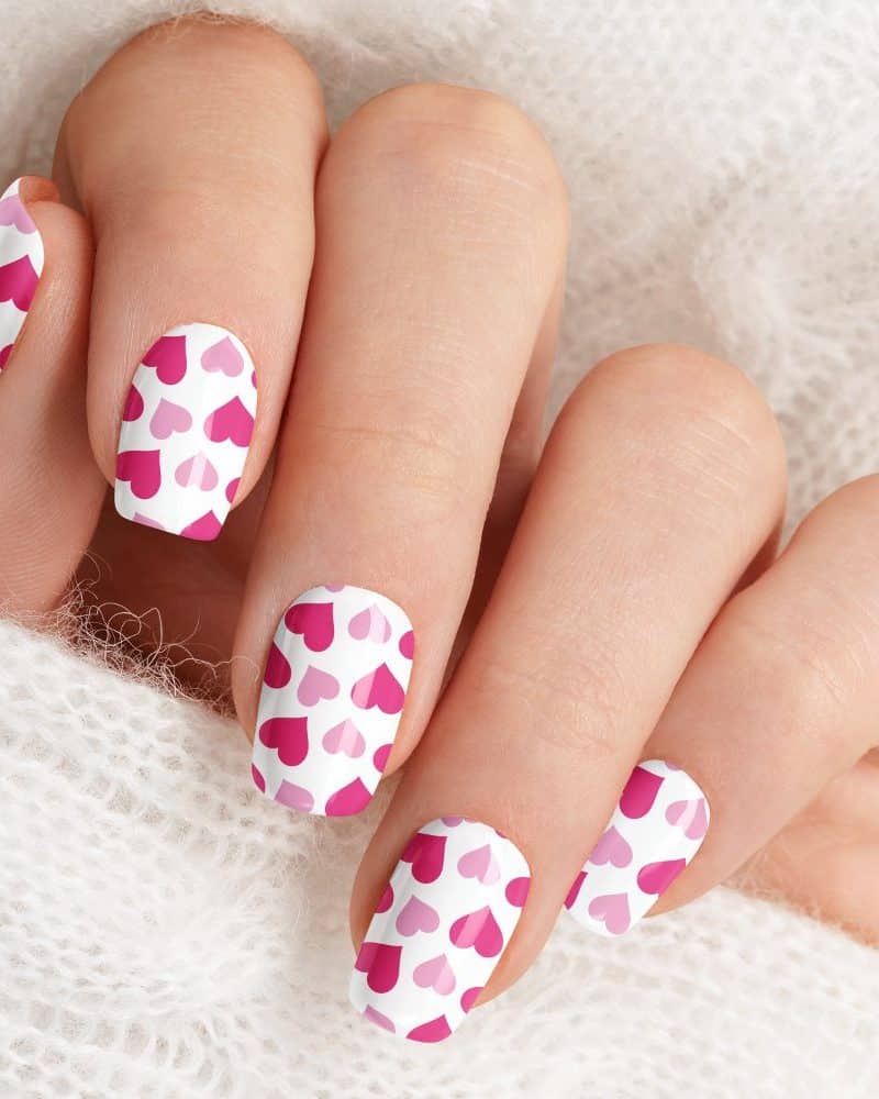 Close-up of a hand with pink and white heart nail art.