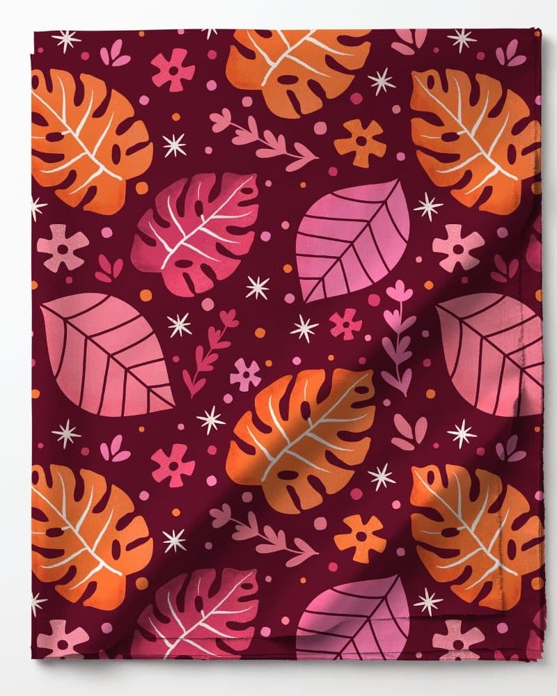 Folded fabric with a repeating pattern of orange and pink leaves and small flowers on a maroon background.