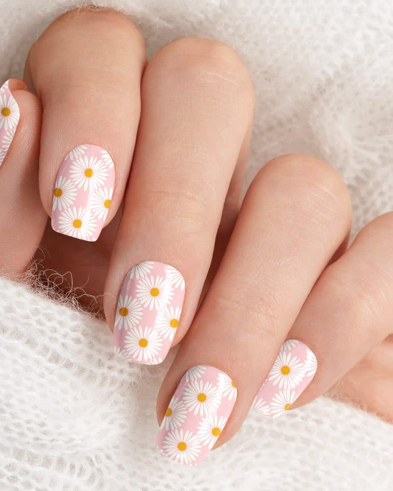 Close-up of a hand with pink daisy nail art.