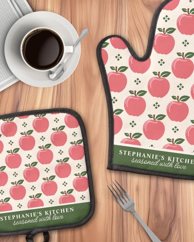 A pair of oven mitts and a pot holder featuring a pink apple pattern and personalized text.