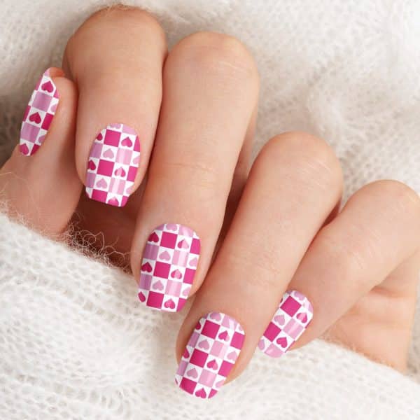 Hand With Fingernails Painted With A Pink And White Checkered Pattern Featuring Small Pink Hearts.