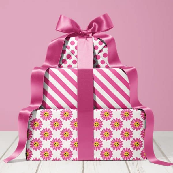 Stack Of Three Pink Presents With A Large Pink Ribbon. The Wrapping Paper Features Different Patterns: Polka Dots, Stripes, And A Daisy And Smiley Face Design.