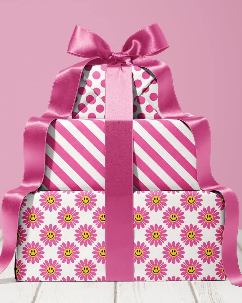 Stack of three pink presents with a large pink ribbon. The wrapping paper features different patterns: polka dots, stripes, and a daisy and smiley face design.