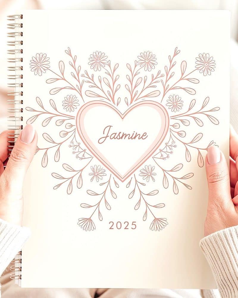 Hands holding a 2025 planner featuring a floral heart design and the name Jasmine.