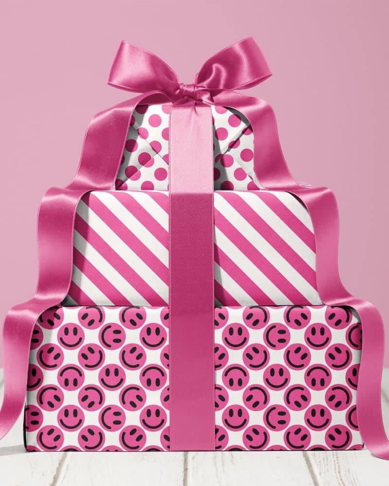 Stack of three pink presents with a large pink ribbon. The boxes are wrapped in patterns of polka dots, stripes, and smiley faces.