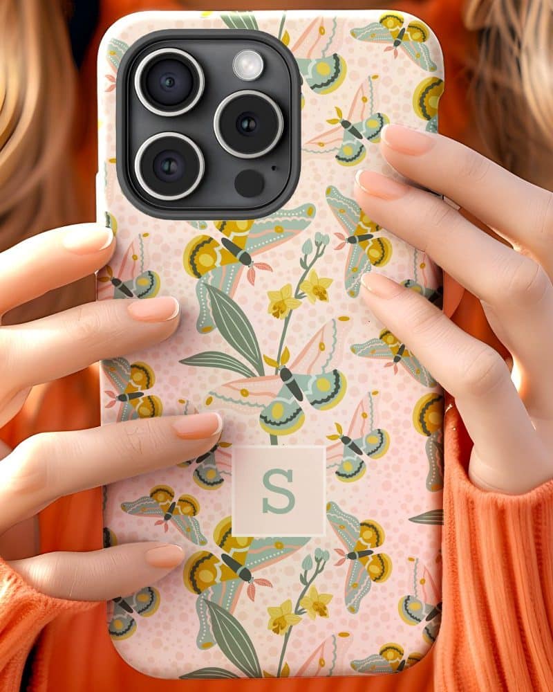 Woman's hands holding a phone case with a pastel butterfly and floral pattern and the initial S.