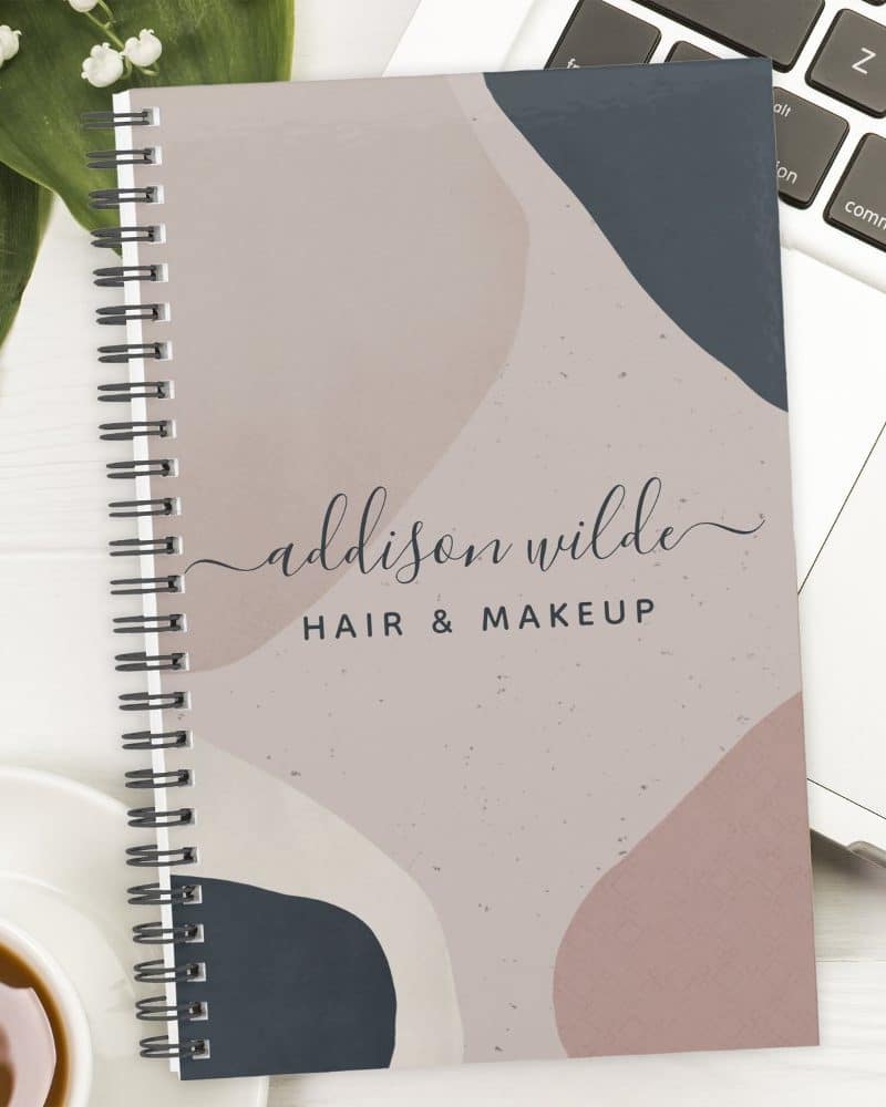 Spiral-bound notebook with an abstract design in muted pink, beige, and blue featuring the name Addison Wilde Hair & Makeup.