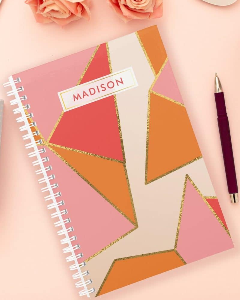 Spiral-bound notebook with a pink, orange, and gold geometric design; the name Madison is on the cover.