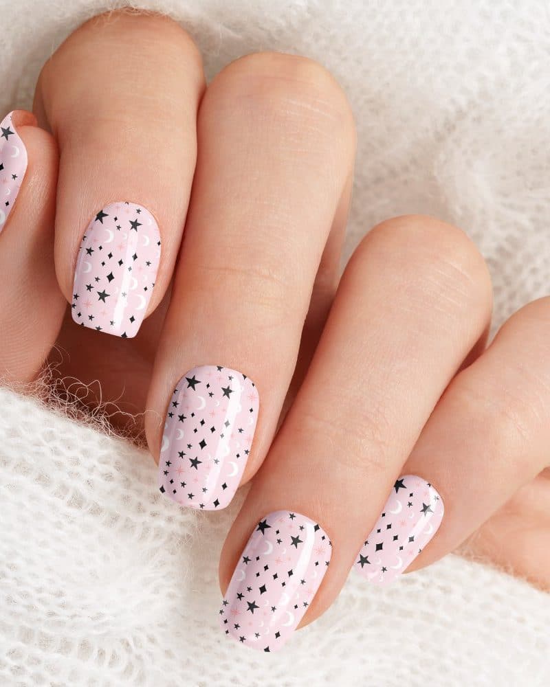 Close-up of a hand with pink nails decorated with a pattern of small stars and crescent moons.