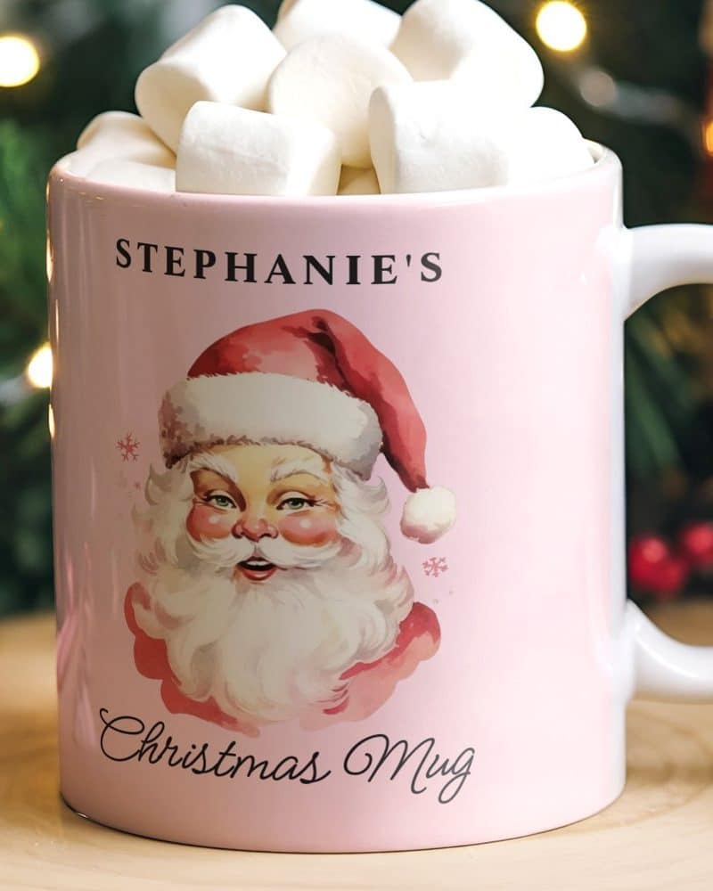 Pink mug with Santa Claus illustration, personalized with the name Stephanie's and the words Christmas Mug. The mug contains marshmallows.