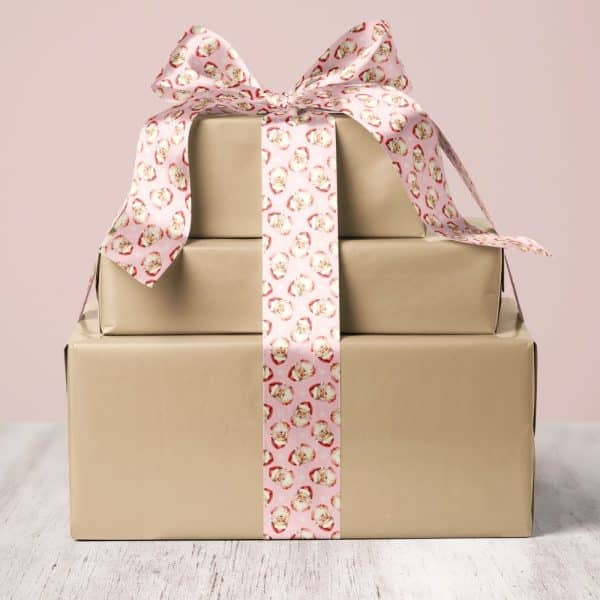 A Stack Of Three Brown Gift Boxes Tied With A Pink Ribbon Featuring A Repeating Santa Claus Pattern.