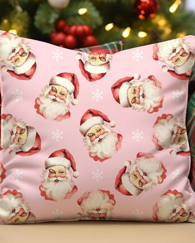 Pink pillow with repeating pattern of Santa Claus faces and snowflakes.