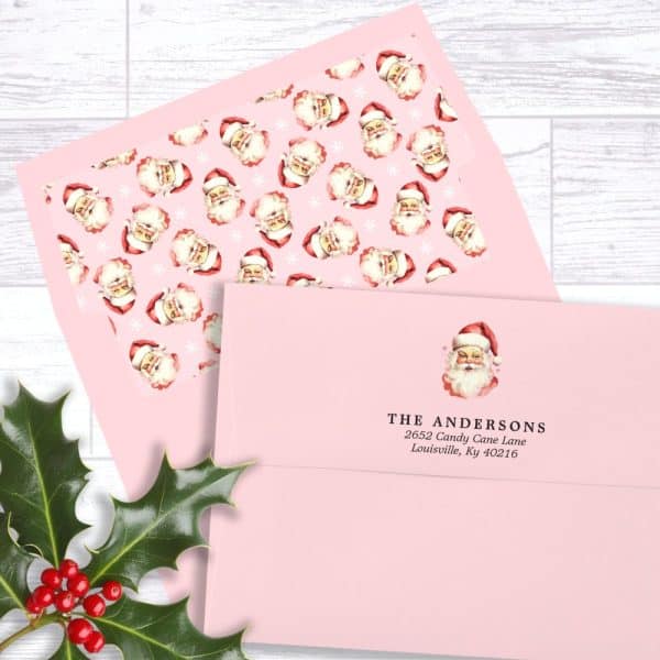 Pink Envelope With A Return Address Label Featuring A Vintage Santa Claus Illustration And The Andersons Family Name And Address. A Piece Of Pink Paper With A Repeating Santa Pattern Is Also Visible.