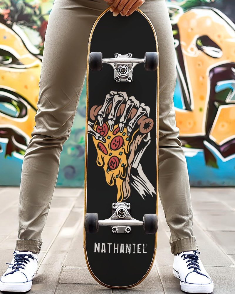 Person holding a black skateboard with a graphic of a skeleton hand holding a dripping pizza slice. The name Nathaniel is printed on the board.