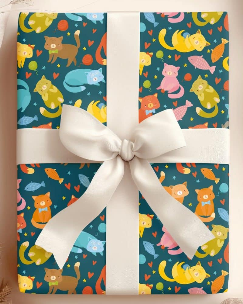 Gift wrapped in teal paper featuring a repeating pattern of colorful cartoon cats and fish, tied with a white ribbon.