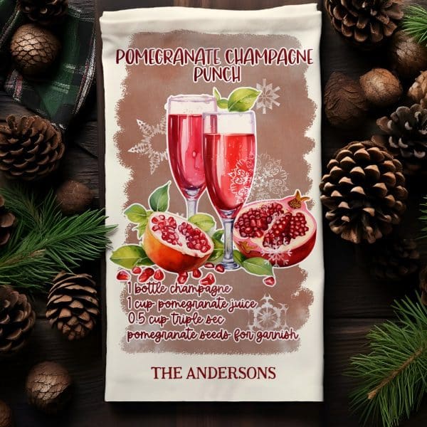 A Kitchen Towel With A Watercolor Illustration Of Two Champagne Flutes Filled With Pomegranate Punch, Accompanied By Pomegranates And A Recipe.
