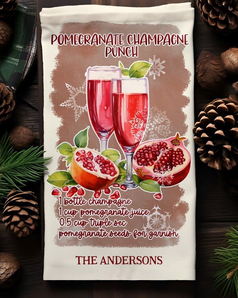 A kitchen towel with a watercolor illustration of two champagne flutes filled with pomegranate punch, accompanied by pomegranates and a recipe.
