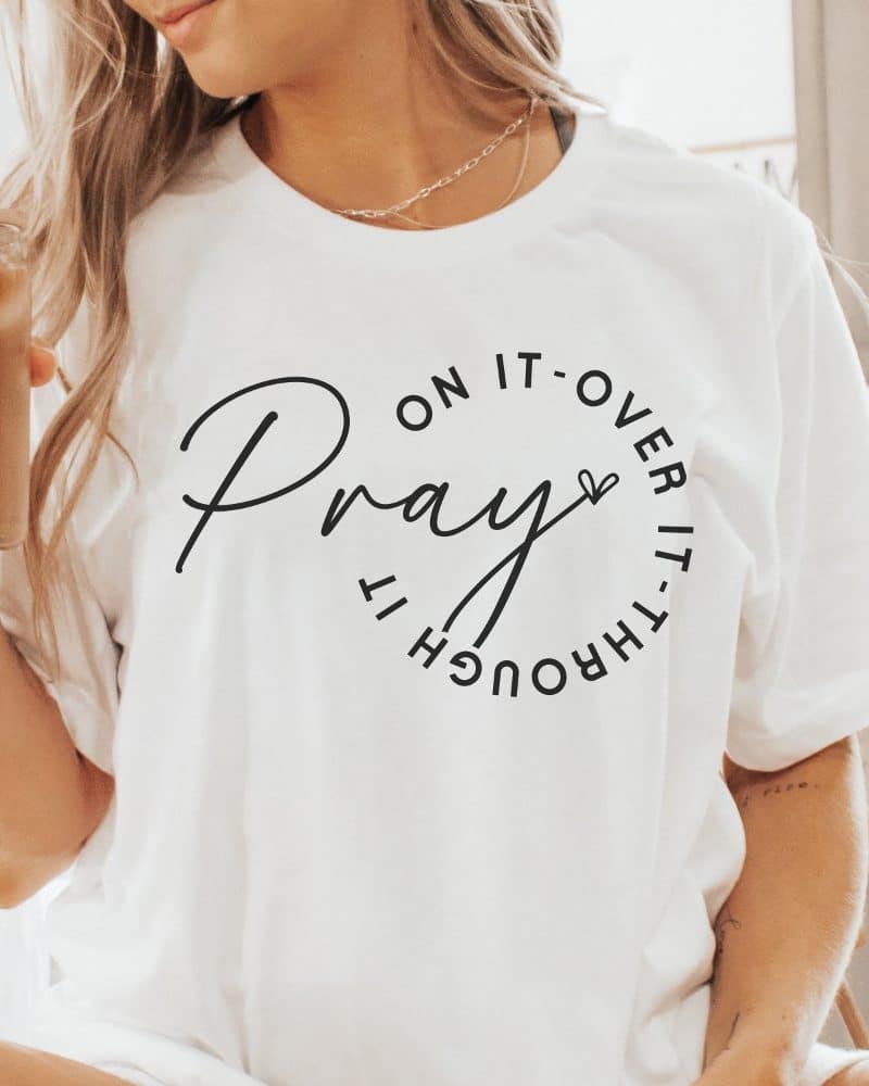 Woman wearing a white t-shirt with the word Pray encircled by the phrase on it over it through it.