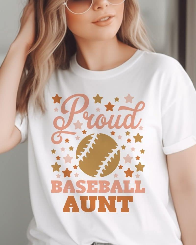Woman wearing a white t-shirt that says Proud Baseball Aunt, surrounded by stars and a baseball graphic.