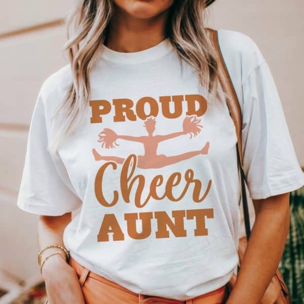 Woman Wearing A White T-Shirt That Says Proud Cheer Aunt With A Graphic Of A Cheerleader.