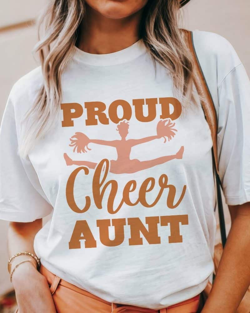 Woman wearing a white t-shirt that says Proud Cheer Aunt with a graphic of a cheerleader.
