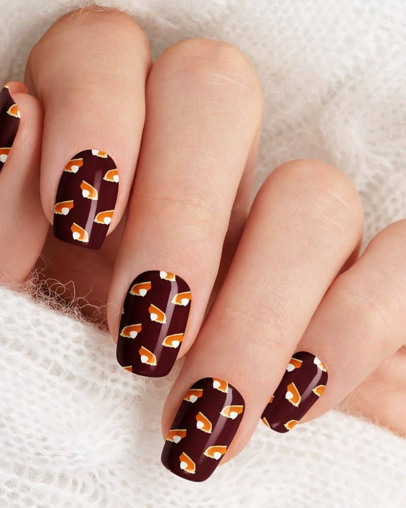 Close-up of a hand with fingernails painted dark brown and decorated with a pattern of small pumpkin pie images.