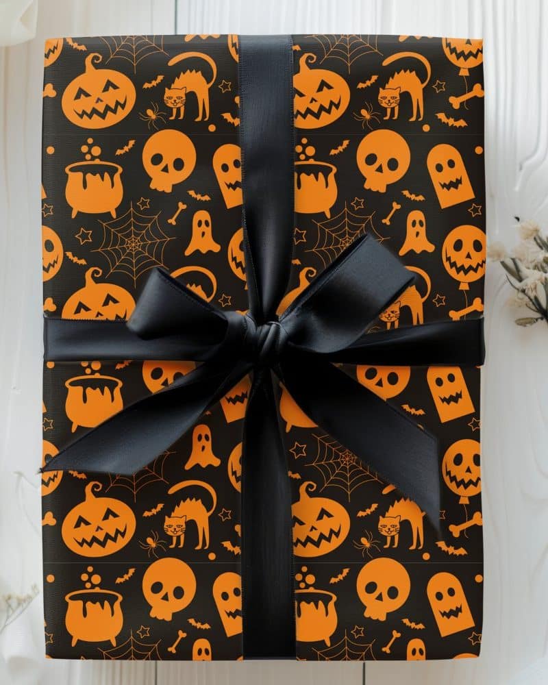 Halloween gift wrapped in black paper with an orange pattern of pumpkins, skulls, and other Halloween icons, tied with a black ribbon.