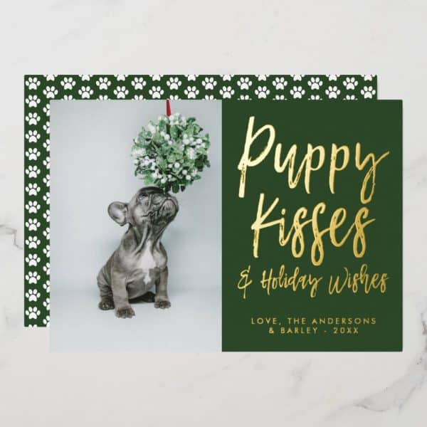 A Christmas Card Featuring A French Bulldog Puppy Looking Up At A Mistletoe Sprig. The Card Is Dark Green With Gold Lettering That Says Puppy Kisses &Amp; Holiday Wishes.