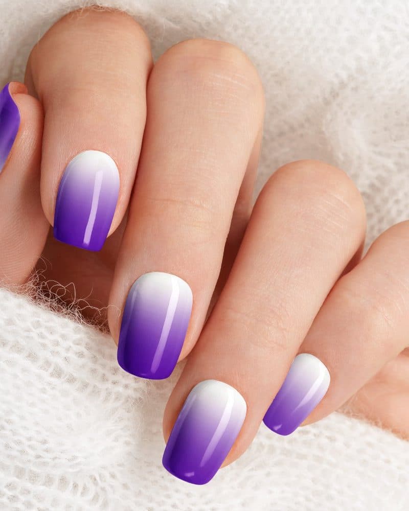 Close-up of a hand with ombre purple and white nails.