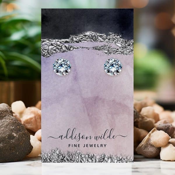 Pair Of Round Brilliant-Cut Diamond Stud Earrings Displayed On A Purple Jewelry Card.