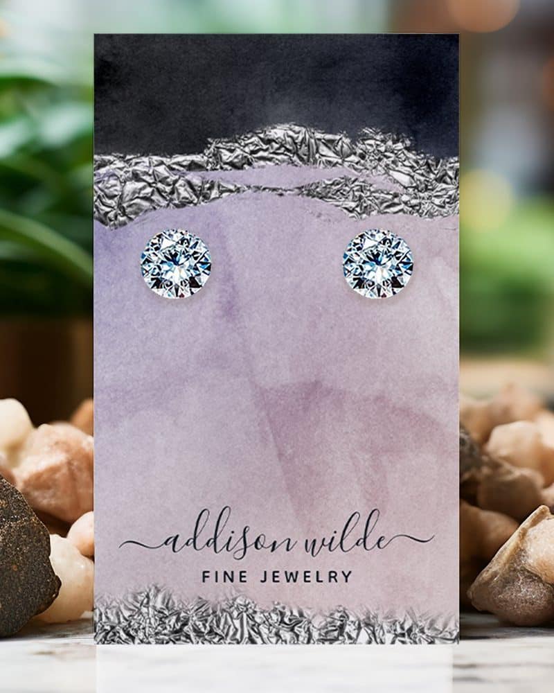 Pair of round brilliant-cut diamond stud earrings displayed on a purple jewelry card.