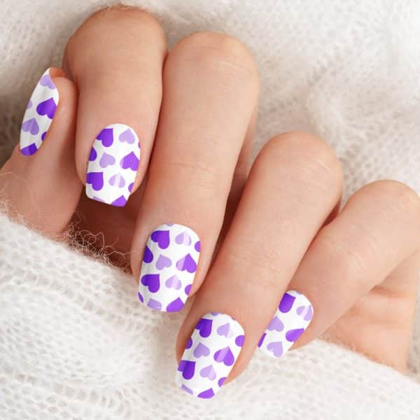 Close-Up Of A Hand With Fingernails Painted With A Pattern Of Purple Hearts On A White Background.