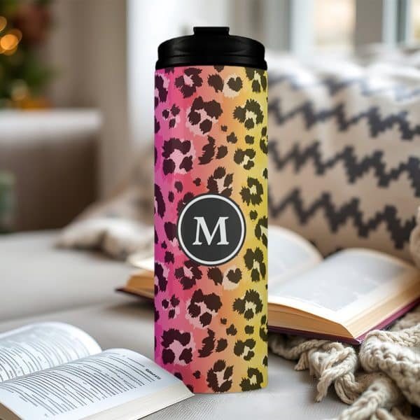Pink, Orange, And Yellow Ombre Leopard Print Travel Mug With A Black Lid And The Letter M In A Circle On The Front.