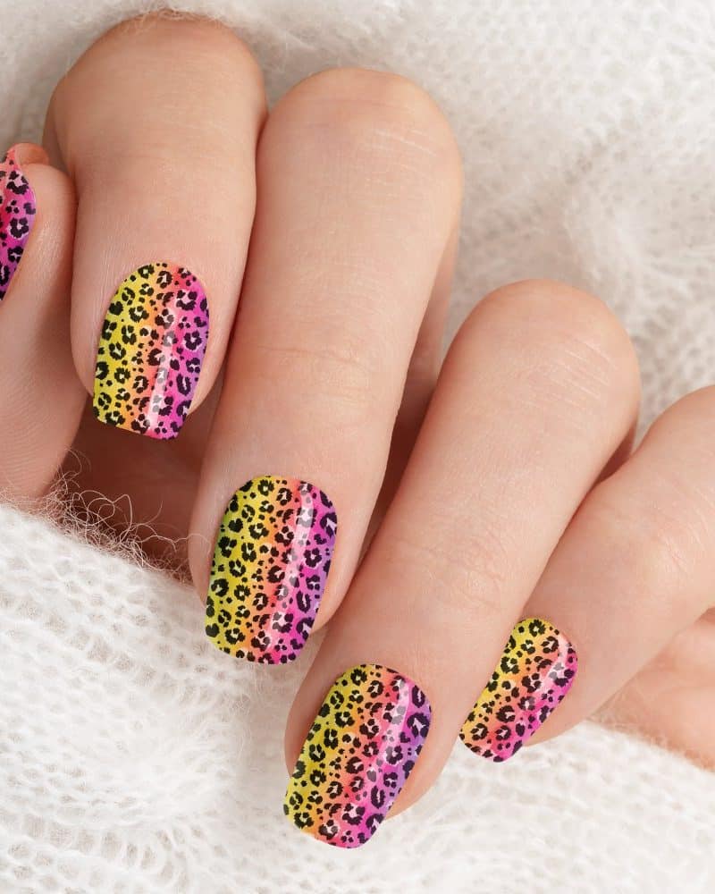 Hand with vibrant ombre leopard print nail art.