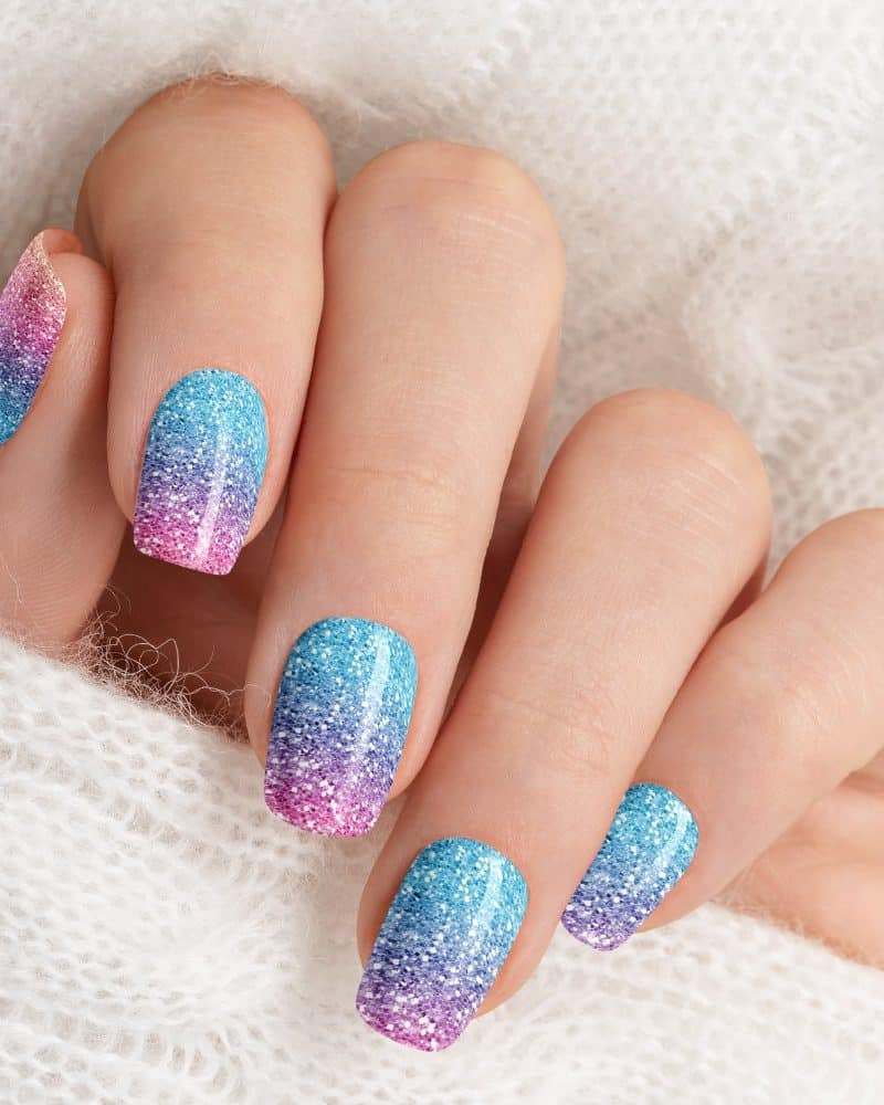 Close-up of a hand with pastel glitter ombre nail polish.
